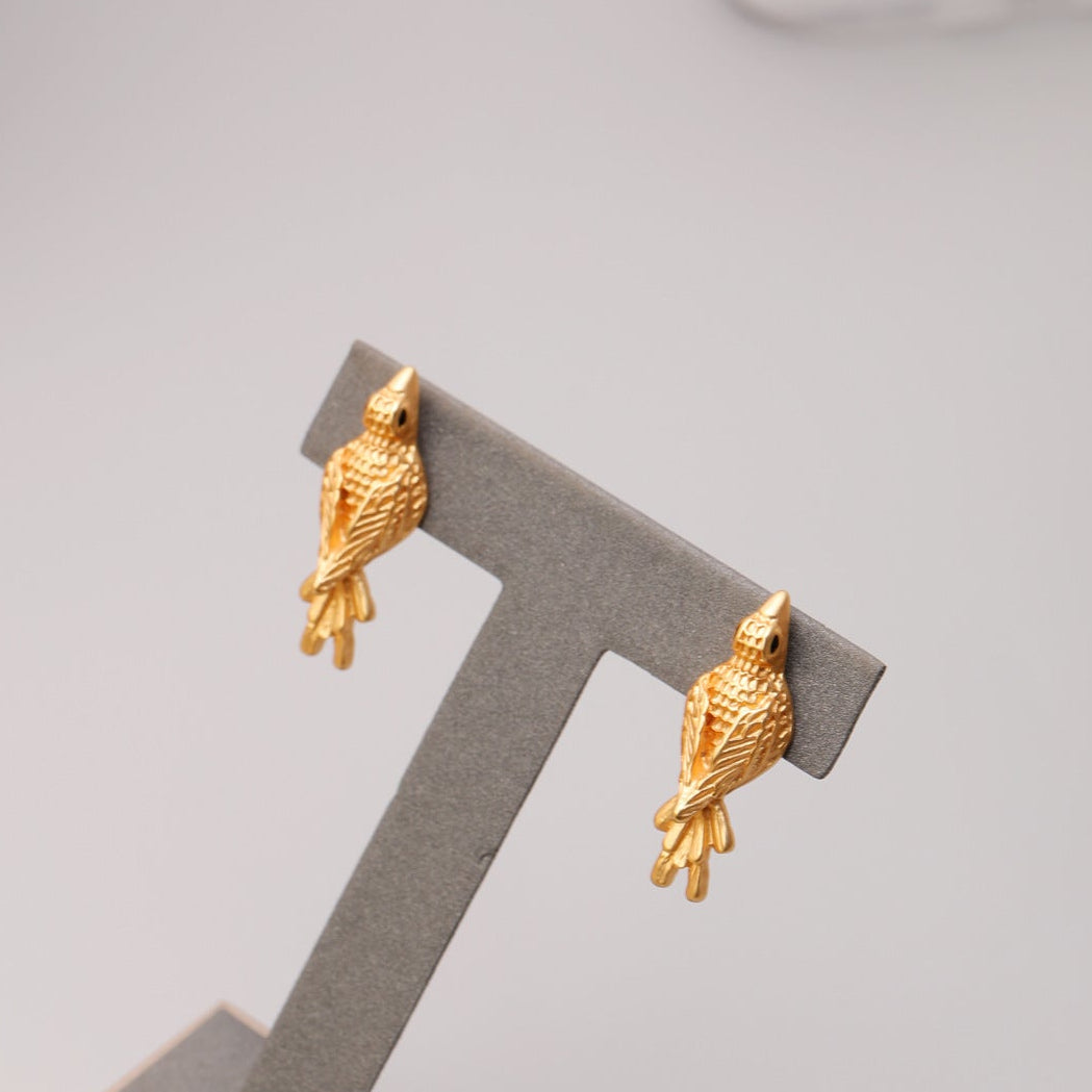 Gold bird-shaped earrings on a jewelry stand.
